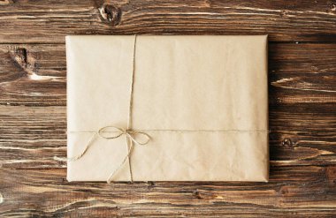 Çevre dostu el sanatları kağıdıyla sarılmış ve sicimle bağlanmış tek bir tatil paketinin genel görünümü. Kırsal ahşap bir masada kare biçimi.