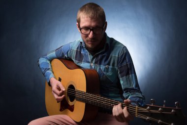 Lacivert arka planda gitar çalan genç müzisyen.