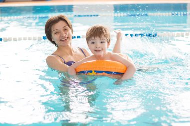 Anne bir çocuğa havuzda yüzmeyi öğretiyor. Sağlıklı aile annesi bebeğe yüzme havuzu öğretiyor.