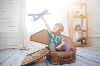 Küçük çocuk model uçakla oynayan bir bavula oturur. Fantezi seyahat konsepti.