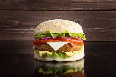 Lezzetli fast food. Marul, peynir, soğan ve domatesli lezzetli hamburgerler siyah arka planda ahşap bir tahta üzerinde