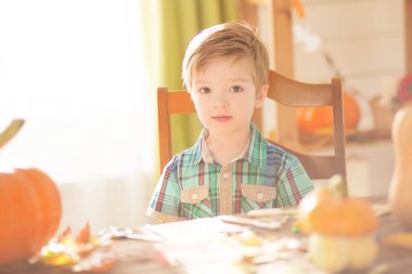 Mutlu Cadılar Bayramı konsepti. Tatlı küçük mutlu çocuk, balkabağı oyuyor ve cadılar bayramını kapalı bir masada kutluyor..