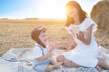Oğluyla havacıda oynayan bir kadın. Aile gün batımında piknikte bir tarlada oturuyor. Mutlu sevgi dolu aile eğleniyor..