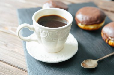 Mini donut ve çikolatalı karamel krema ve sade kahve fincanı, siyah masa tonunda.