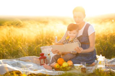 Sevimli erkek çocuk ve güzel hamile annesi güzel bir sonbahar ya da yaz gününde piknikte kitap okuyorlar. Mutlu aile ve eğitim kavramı