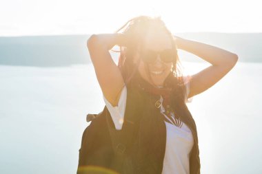 Dağın tepesinde eli cebinde duran bir kadın gün doğumunun altındaki sisli dağ sırasının panoramik manzarasına bakıyor.