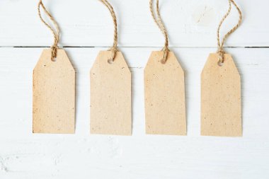 Kahverengi ahşap arka planda dört tane boş karton etiket. Ahşap zemin üzerinde ip olan dört boş etiket..