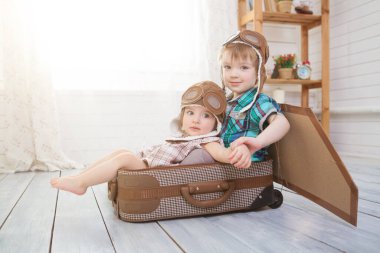 Pilot kostümü giyen ve eski bavulla oynayan iki küçük çocuk. Fantezi seyahat konsepti.