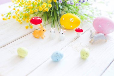 Tavşanlı renkli paskalya yumurtaları ya da ahşap bir masada tavşan oyuncakları ve çiçekler.