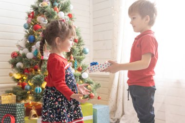 Oğlan, parlak güneşli bir odada bir kıza Noel hediyesi verir..