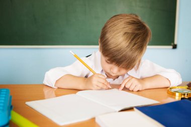Okuldaki küçük şirin çocuk deftere yazıyor.