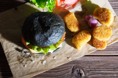 Lezzetli fast food. Tahta üzerinde kraft kağıdı olan siyah ekmekli çizburger.