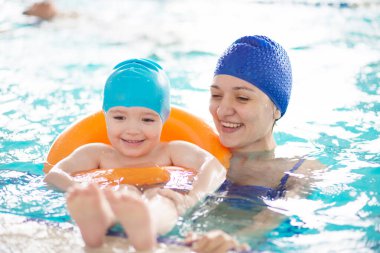 Anneyle bebek havuzda yüzmeyi öğreniyor. Anne oğluna yüzmeyi öğretiyor.