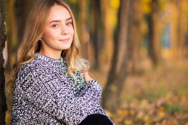 Sonbahar manzarasında gülümseyen genç bir kız. Güz yapraklarıyla çevrili güzel bir bayanın açık hava moda fotoğrafı.