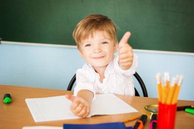 Sevimli okul çocuğu başparmağını kaldırıyor ve okul sezonunun tadını çıkarıyor.