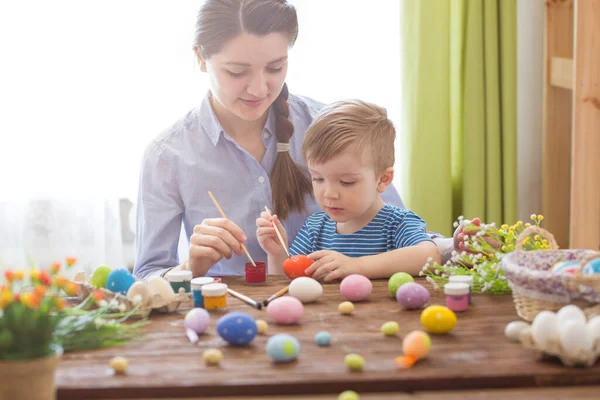 Paskalyayı kutlayan sevimli anne ve oğul. Paskalyayı kutlayan aile. Ebeveyn ve çocuk içeride oynuyorlar. Madalyalı ev ve bahar çiçekleri.