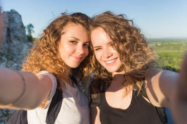 Sınırları olmayan bir dünya. Dağlarda iki kızın çarpıcı yolculuğu. seyahat macera turizmi konsepti. Gülümseyen iki kız uçurumda kendi portresini yapar..