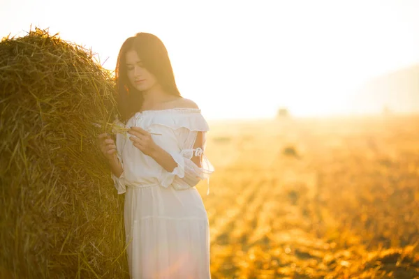 Summer is a great dream time. Beautiful girl in white dress running on the autumn field of wheat at sunset time..