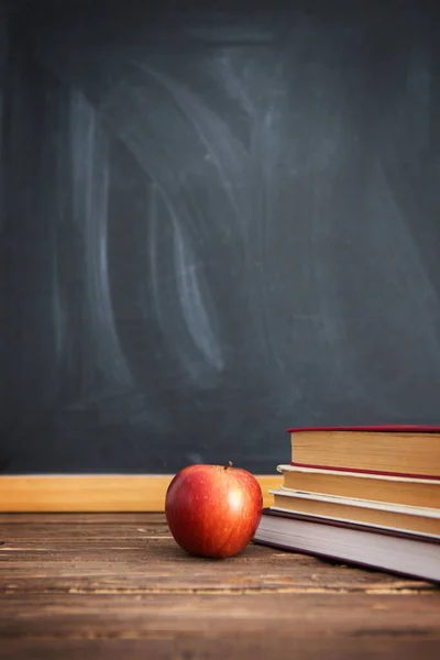Books and apples on a wooden table against the background of the chalkboard or blackboard.