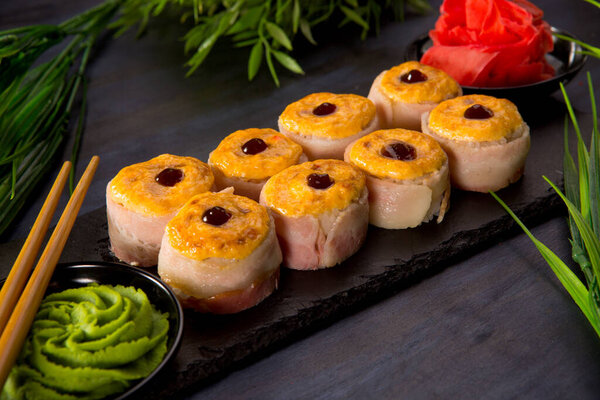 Set of baked sushi rolls with wasabi and ginger on a black background. Japanese oriental cuisine