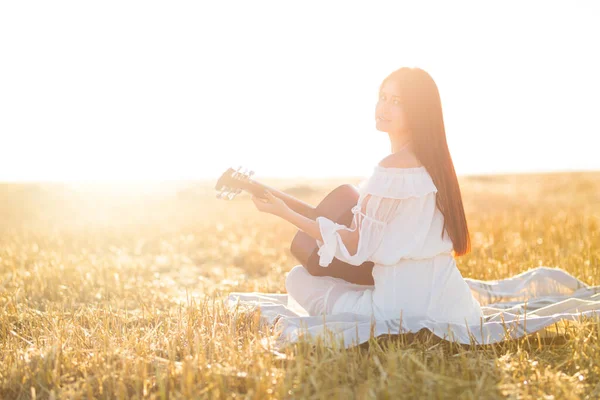 Summer is a great dream time. Country girl sitting with guitar at wheat field.