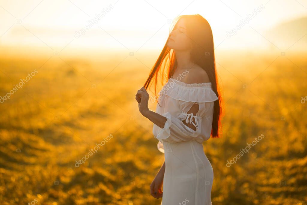 Summer is a great dream time. Young woman on field under sunset light.