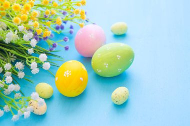 Renkli paskalya yumurtaları ve mavi ahşap masadaki çiçekli dallar..