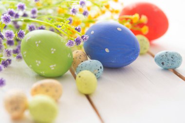 Paskalya yumurtaları ve bahar çiçekleri beyaz kırsal ahşap arka planda.