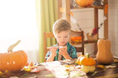 Mutlu Cadılar Bayramı konsepti. Tatlı küçük mutlu çocuk, balkabağı oyuyor ve cadılar bayramını kapalı bir masada kutluyor..