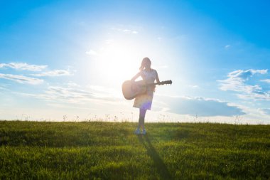 Bulutlu gün batımında ya da gündoğumunda elinde gitar tutan güzel sarışın kadın ve yeşil arka plan Yazıtlar için Boşluğu Kopyala