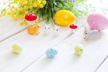 Tavşanlı renkli paskalya yumurtaları ya da ahşap bir masada tavşan oyuncakları ve çiçekler.