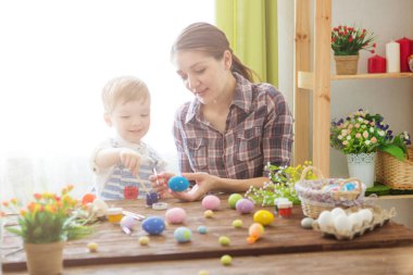 Paskalya hazırlıkları. Mutlu genç anne, neşeli oğluyla vakit geçiriyor. Mutlu aile anne ve çocukları Paskalya yumurtalarını renklerle boyarlar. Paskalya tatili için hazırlık.