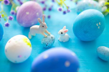 Mavi ahşap bir masada paskalya yumurtaları. Yumurta ve çiçekler oyuncak Paskalya tavşanı.