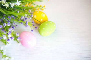 Ahşap masada renkli paskalya yumurtaları ve çiçekler.