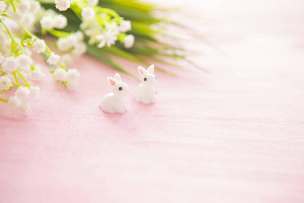 Easter bunny statuettes and flowers on wooden background.