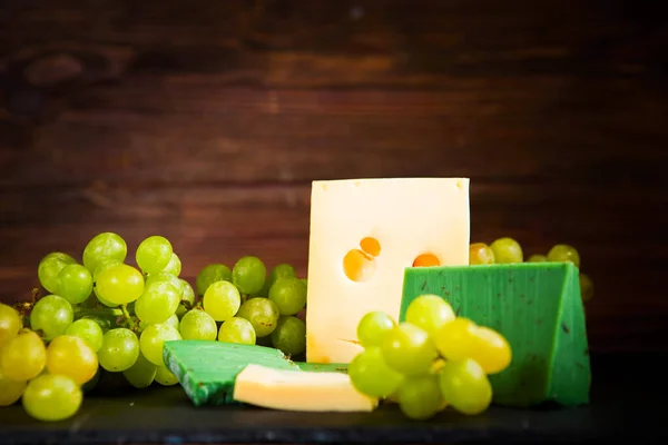 木製テーブルの上に黒スレートのチーズボード上のチーズと緑のブドウのショット — ストック写真