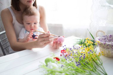 Küçük çocuk ve annesi evde paskalya yumurtalarını boyuyor. Anne oğluna Paskalya yumurtalarını nasıl süsleyeceğini öğretiyor..