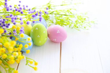 Beyaz ahşap masadaki çiçeklerle renkli paskalya yumurtalarını kapatın. Boşluğu kopyala