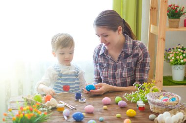Paskalyayı kutlayan sevimli anne ve oğul. Paskalyayı kutlayan aile. Ebeveyn ve çocuk içeride oynuyorlar. Madalyalı ev ve bahar çiçekleri.