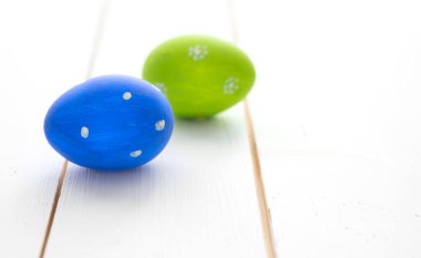 Beyaz ahşap masa arkasında iki renkli paskalya yumurtası. Mavi ve yeşil.