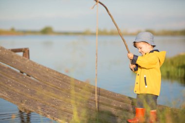 Little Boy Catching a Fish from wooden dock. Summertime clipart
