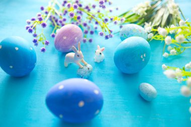 Mavi ahşap bir masada paskalya yumurtaları. Yumurta ve çiçekler oyuncak Paskalya tavşanı.