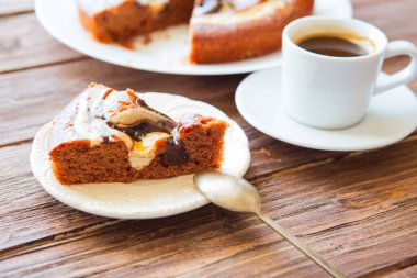 Beyaz tabakta nefis çikolatalı pasta ve bir parça çikolatalı kek. Ahşap masa arkasında bir fincan kahve, yakın plan..
