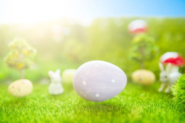 Mutlu Paskalyalar. Bahar yeşili çimlerde bebek Paskalya tavşanı. Plastik yeşil tarlada günbatımında plastik çimenler, mantarlar ve ağaçlar. Sahte ot. Makro.