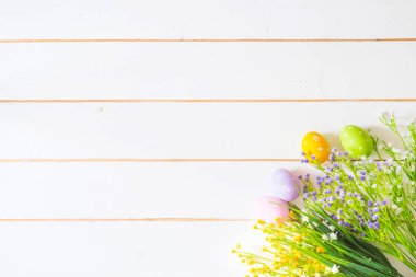 Beyaz ahşap bir masada bahar çiçekleri ve paskalya yumurtaları. Yukarıdan görüntüle.
