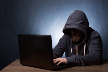 Kapüşonlu bilgisayar korsanı laptopla bilgi çalıyor.