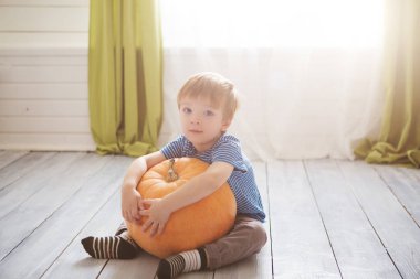 Harika küçük çocuk büyük balkabağıyla oturuyor. Çocuklar Cadılar Bayramı 'nı oturma odasında kutluyorlar..