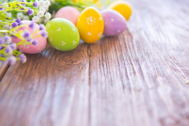 Kahverengi ahşap arka planda kır çiçekleri olan Paskalya yumurtaları.
