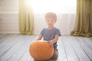 Harika küçük çocuk büyük balkabağıyla oturuyor. Çocuklar Cadılar Bayramı 'nı oturma odasında kutluyorlar..