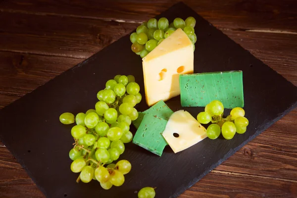 Tiro Queijo Uvas Verdes Placa Queijo Ardósia Preta Mesa Madeira — Fotografia de Stock